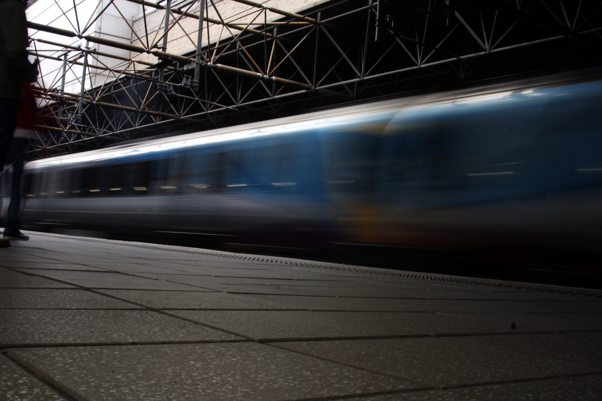 A train streaking through the station in a long-exposure blur, the platform sharp in the foreground