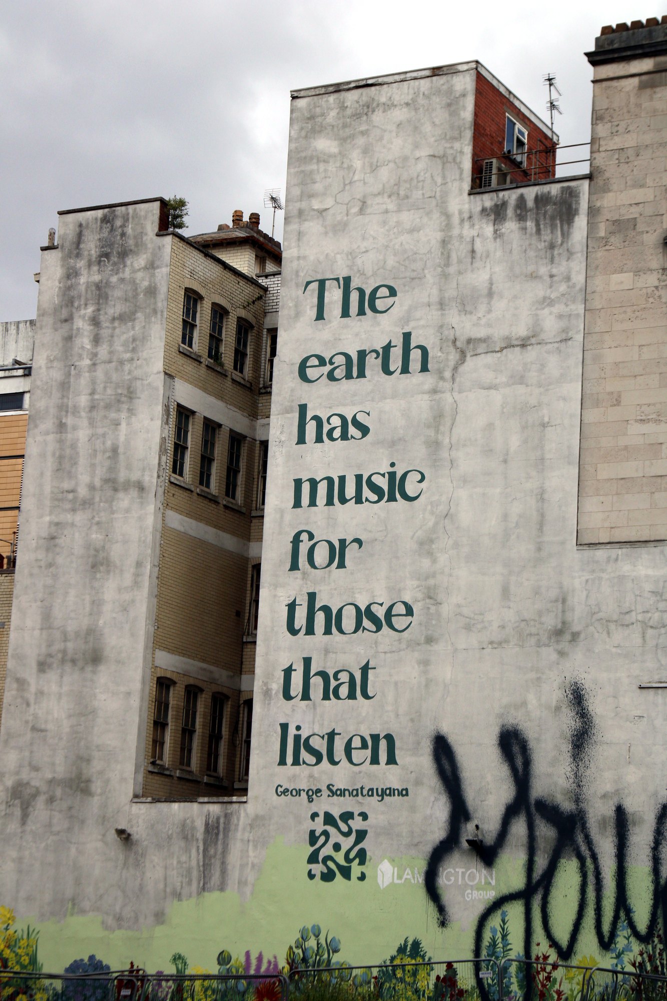 Painted wall reading ‘The earth has music for those that listen’ above layers of graffiti