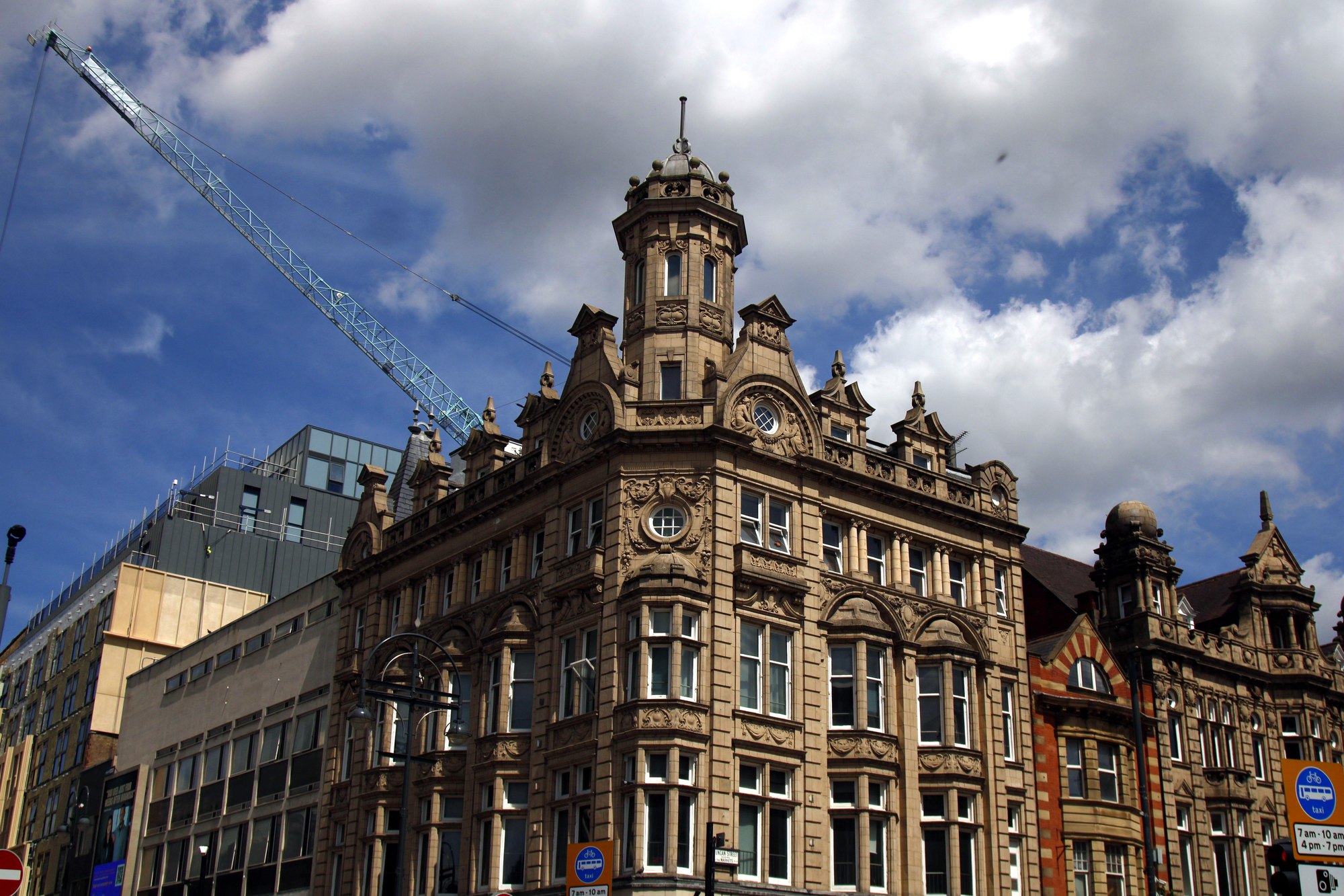 Ornate Victorian corner building under a blue sky, a crane rising behind it