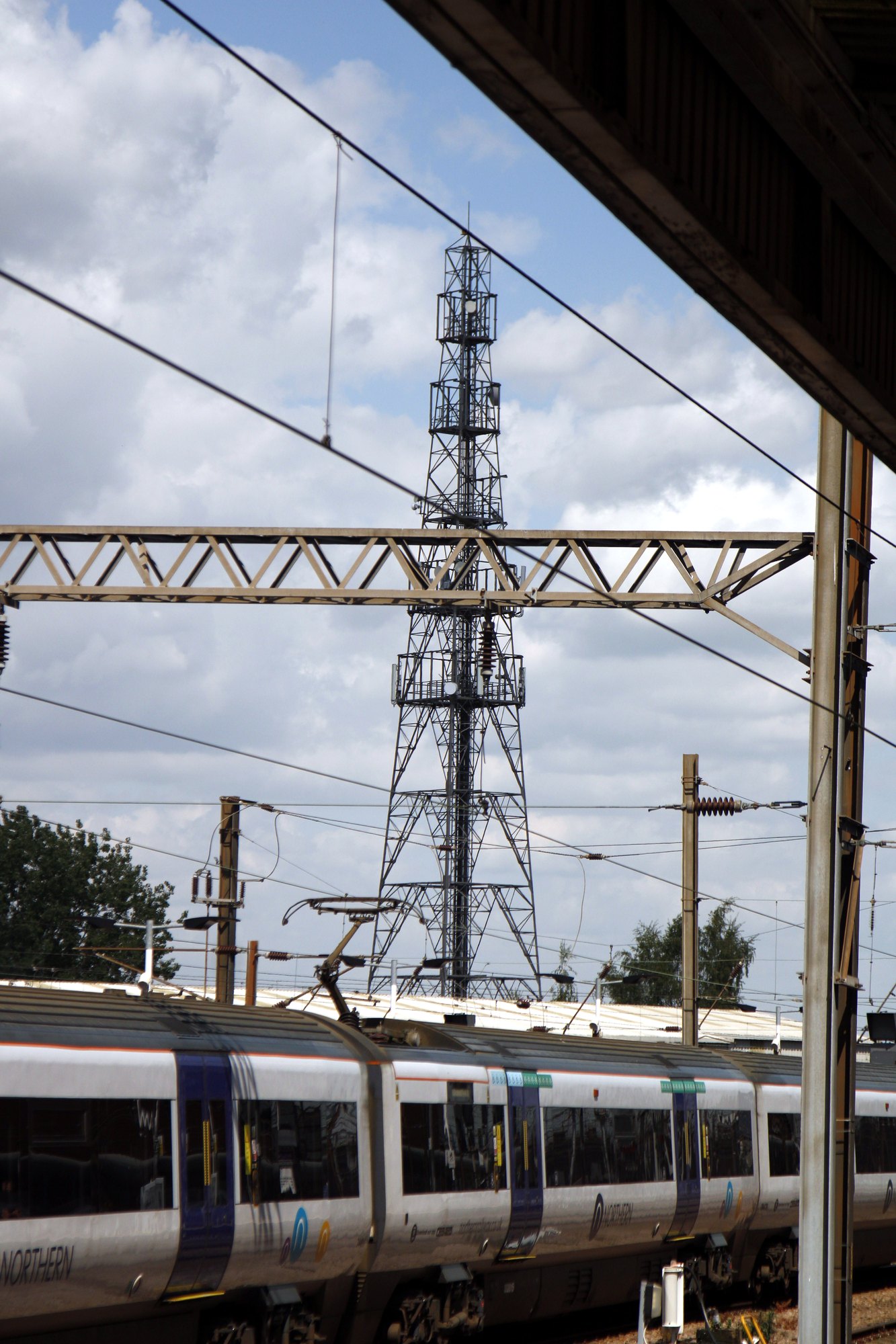 Railway mast and overhead wires above a passing commuter train