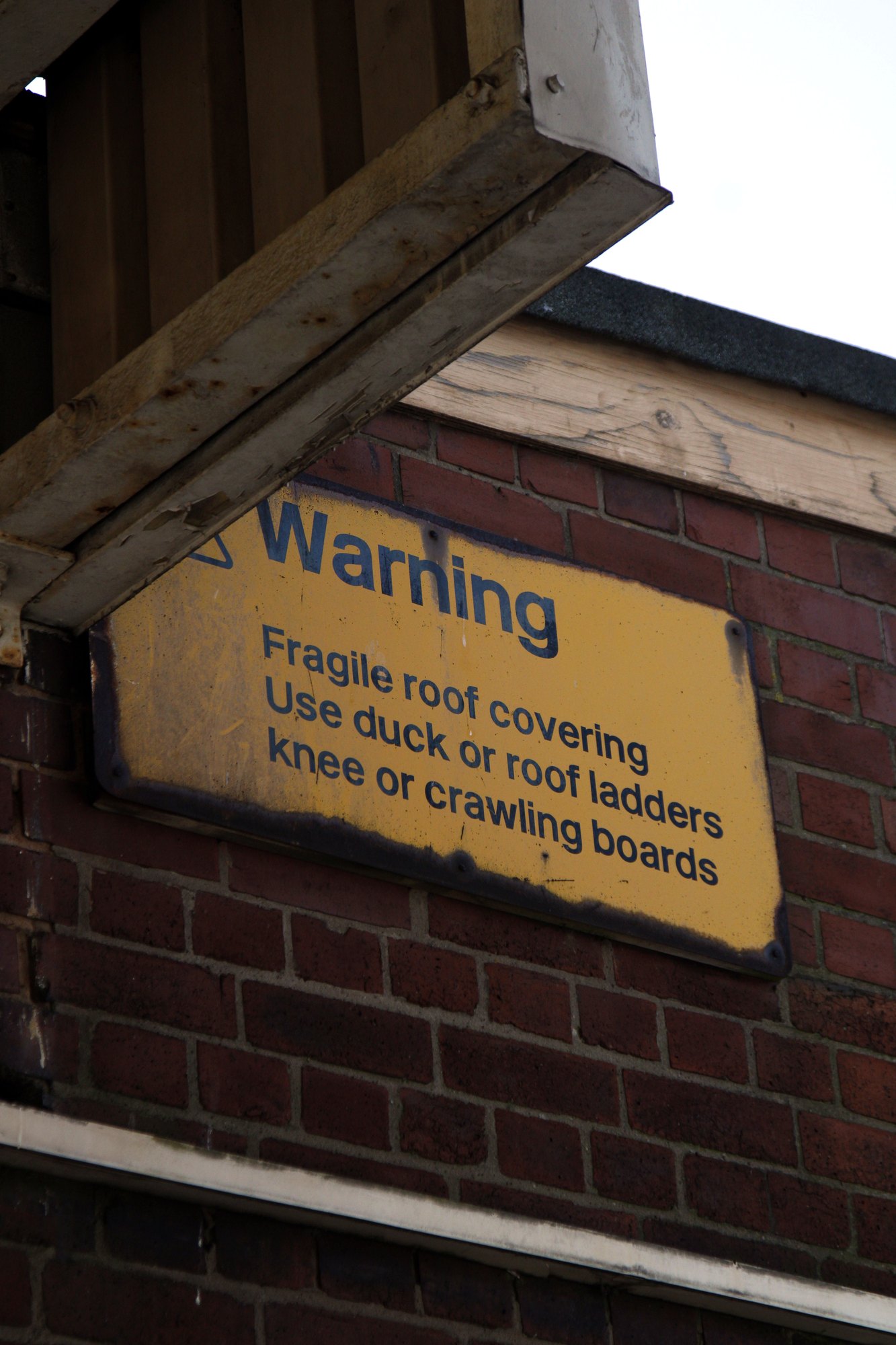 Yellow warning sign about a fragile roof on an old brick wall