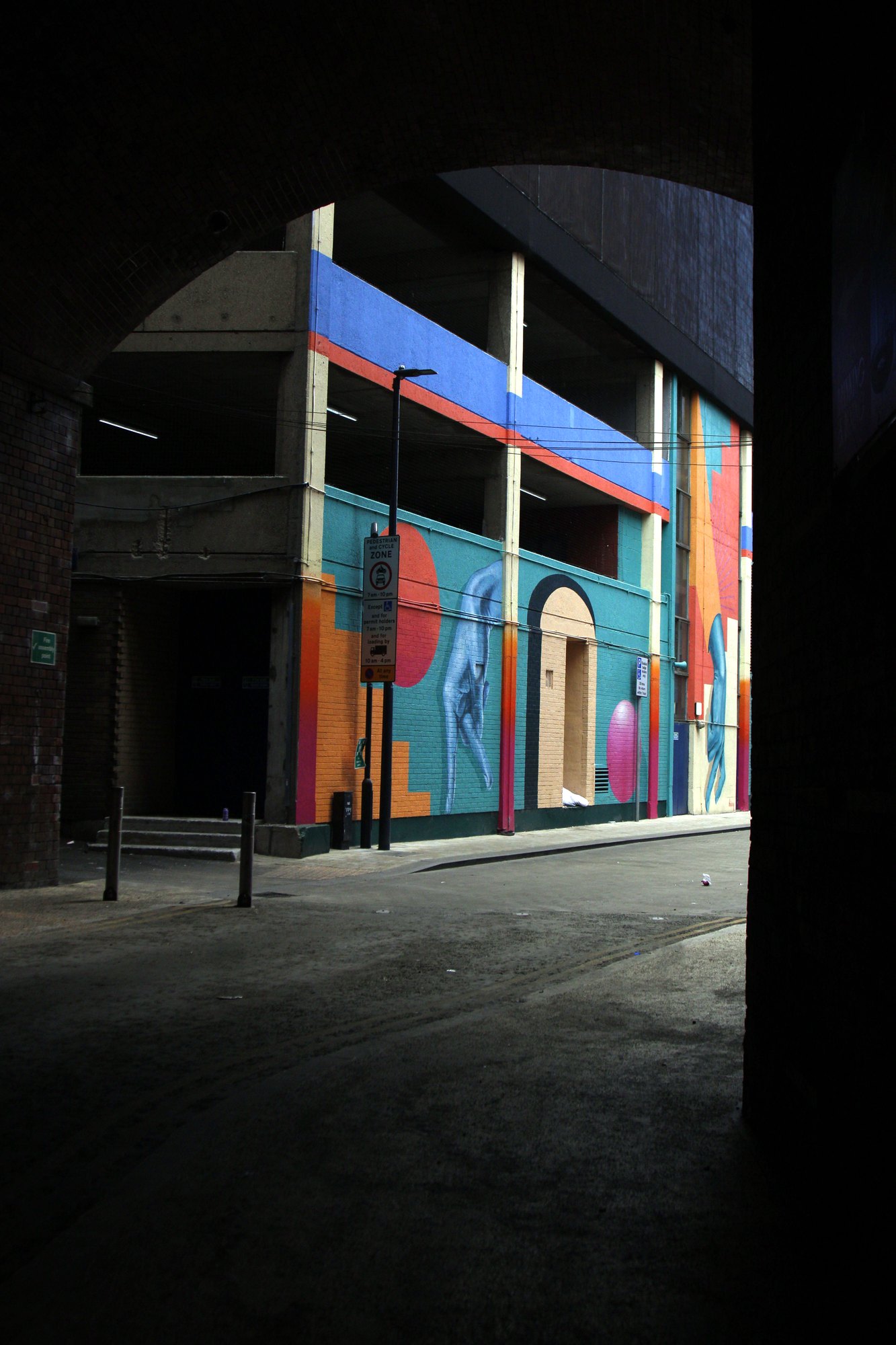 Colourful mural seen through a dark archway at the end of an empty alley