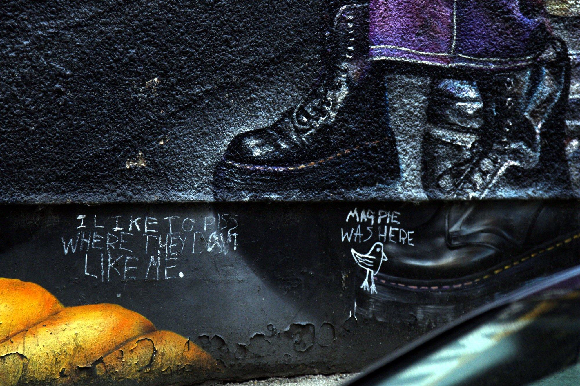 Mural of a giant boot above chalk writing on a dark wall