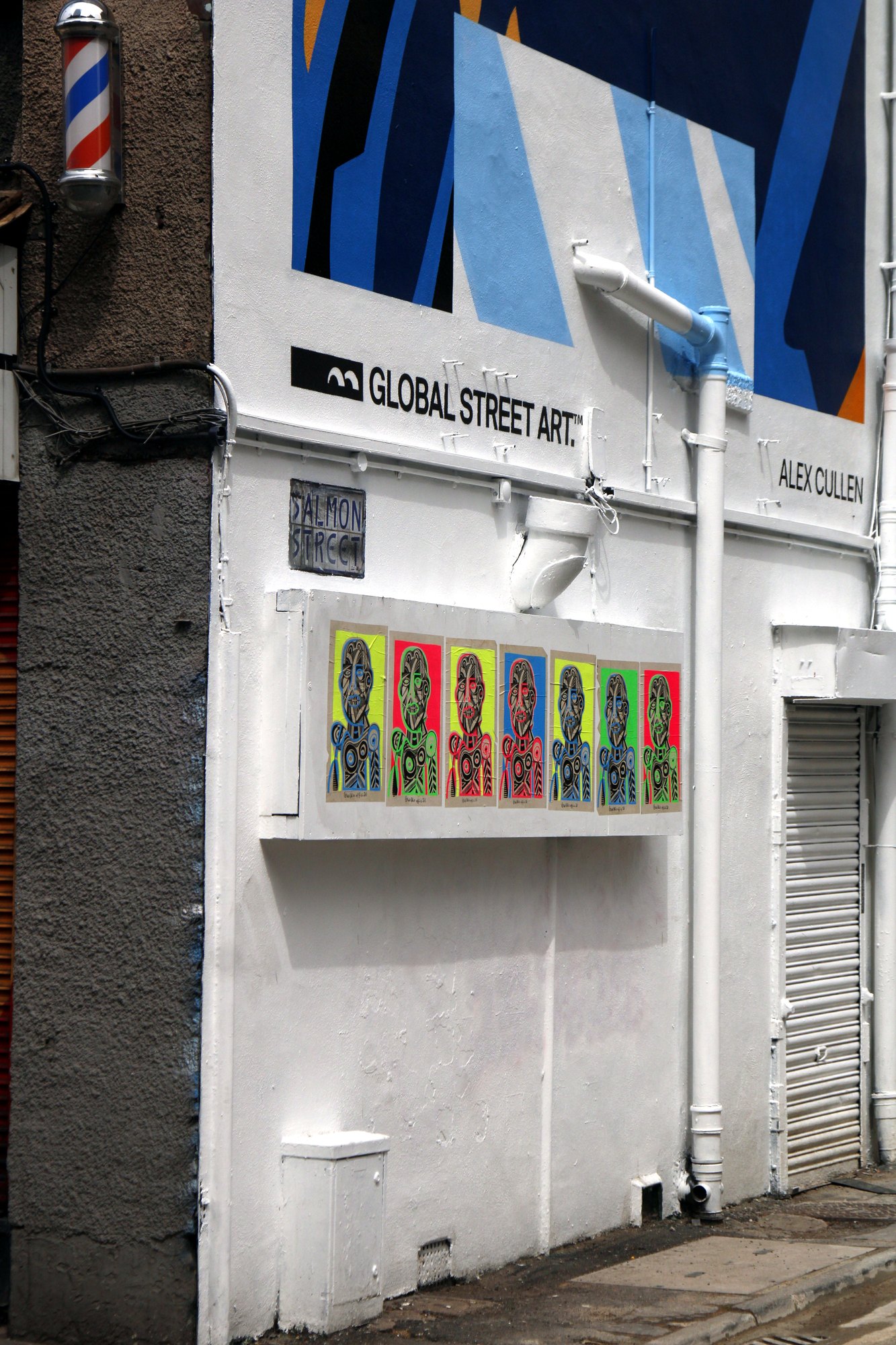 White-painted street art gallery wall with a row of bright portraits