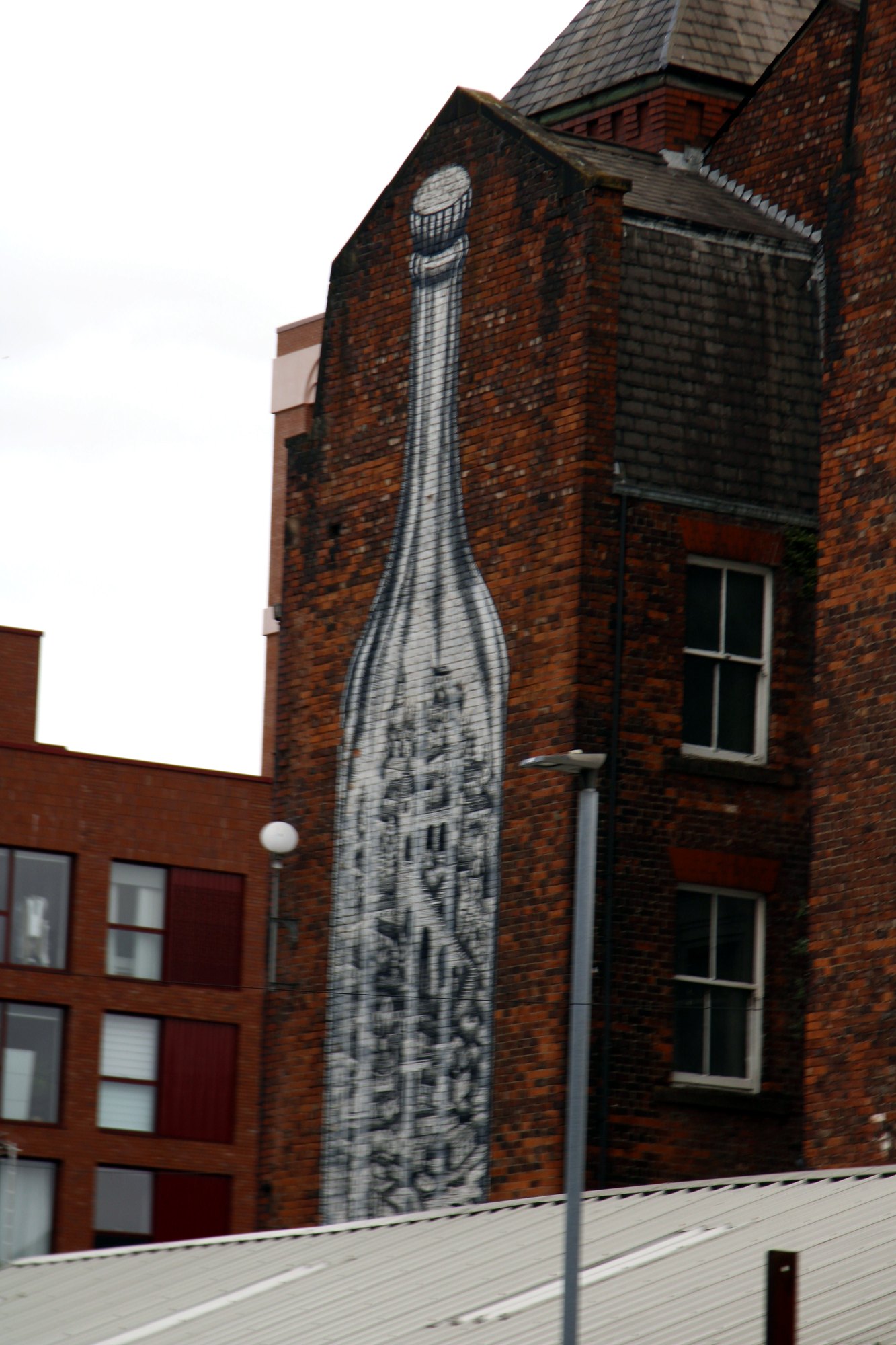 Tall mural of a bottle painted up the side of a red-brick building