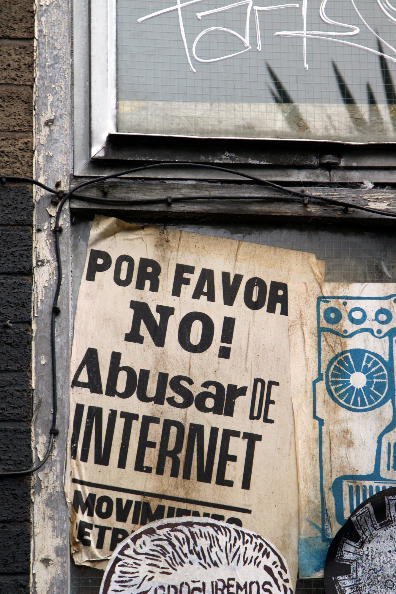 Weathered poster reading ‘Por favor no! Abusar de internet’ under a tagged window