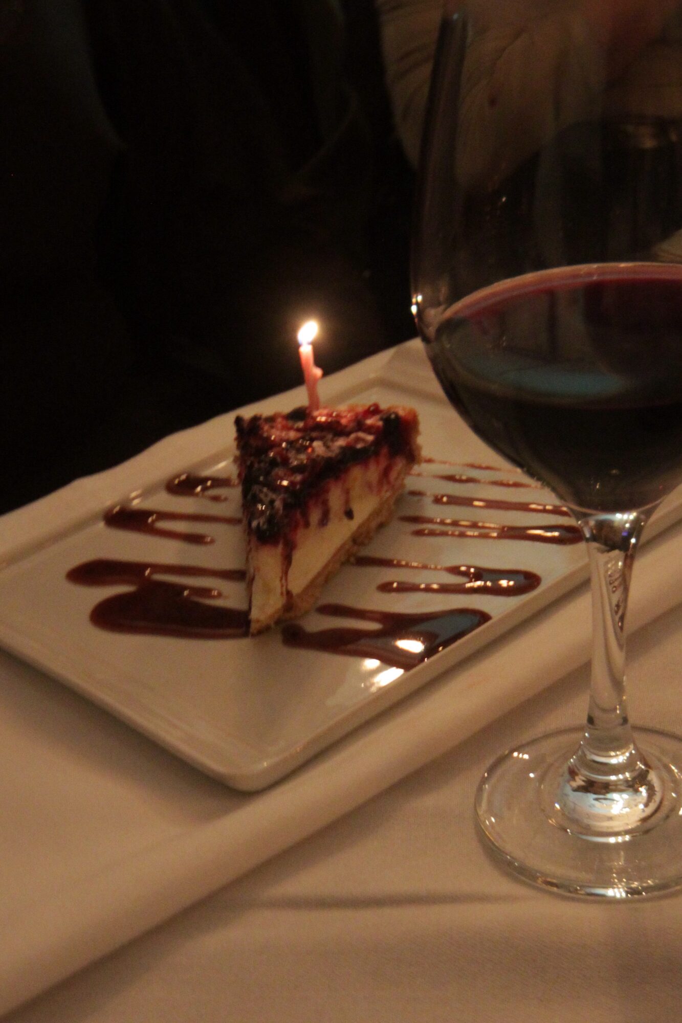 Dessert with candle beside a glass of red wine